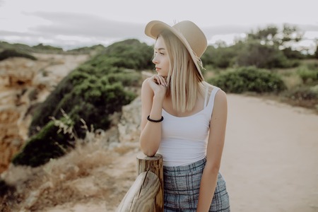 Young woman in straw hat standing on the view point of seacost with stone beach on background
