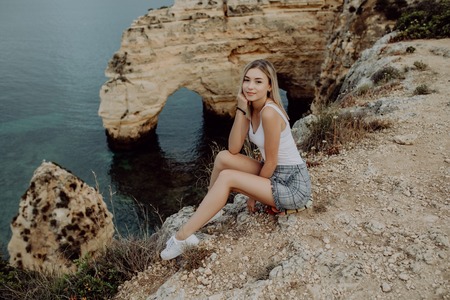Latin Girl sitting on a cliff and enjoy the summer time near Atlantic ocean in Portugalの写真素材