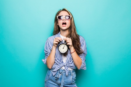 Portrait of young shocked irritated woman student with backpack clinging to head, hold alarm clock...