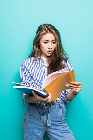Portrait of beautiful young brunette holding notebooks isolated on the blue backgroundの写真素材