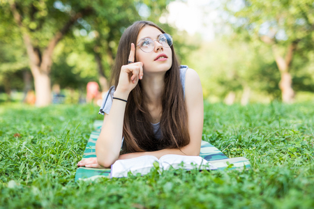 Concentrated young woman resting with book in park. Serious beautiful girl lying on grass while reading favorite romance.の写真素材