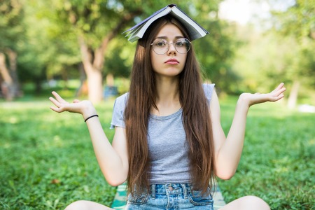 Portrait of a beautiful funny cute happy young lady girl student sitting in park outdoors on green...