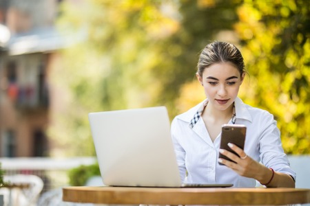Image of happy woman using laptop and smartphone in cafe. Young beautiful girl sitting in a coffee...