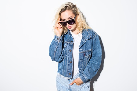 Pretty young woman dressed in hipster style jeans short posing on white wall background