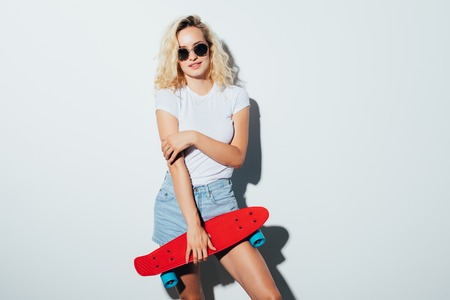 Hipster girl in holding a skateboard and looking at the camera isolated on whiteの写真素材