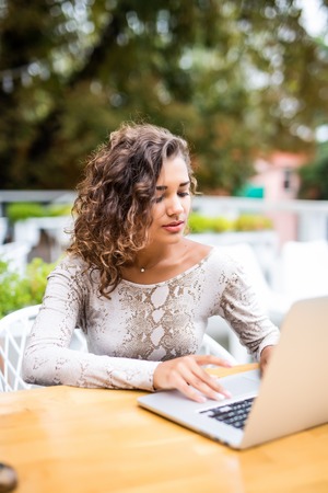 Beautiful young curly latin woman with an afro hairstyle working at her laptop in a coffee shop