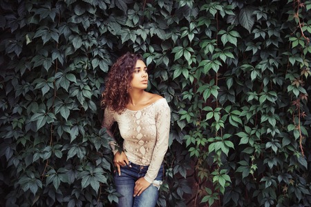 Portrait of young beauty curly latin woman posing near leaves wallの写真素材