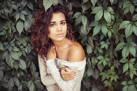 Portrait of young beauty curly latin woman posing near leaves wallの写真素材