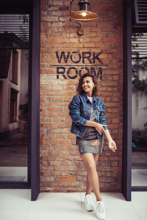 Beautiful latin curly woman portrait, smiling and looking at camera against brickの写真素材