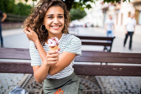 beautiful business woman in a long dress sitting on a park bench and eating ice cream in the summerの写真素材