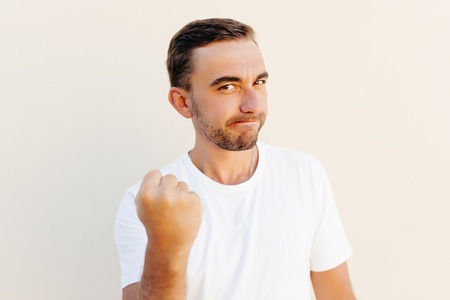 Closeup portrait, angry cranky upset young man, worker, business putting up fist about to give you knuckle sandwich, isolated orange background.の写真素材