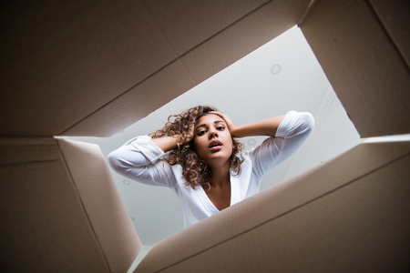 Surprised young female opening a carton box and looking peering inside with widely opened eyesの写真素材