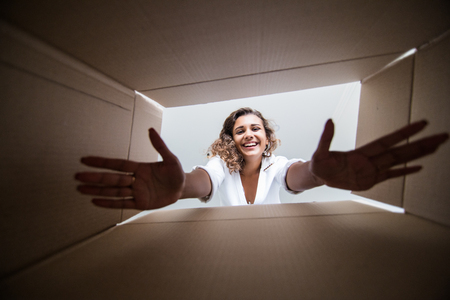 Smiling young woman opening a carton box, relocation and unpacking conceptの写真素材
