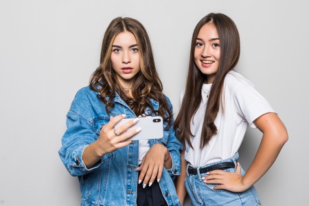 Two girlfriend with phone in hands looking at camera isolated on grayの写真素材