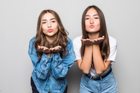 Portrait of two beautiful young girls blowing kisses to camera isolated on the white backgroundの写真素材