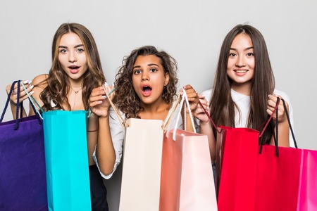 Three beautiful shocked women looking inside shopping bags isolated over gray backgroundの写真素材