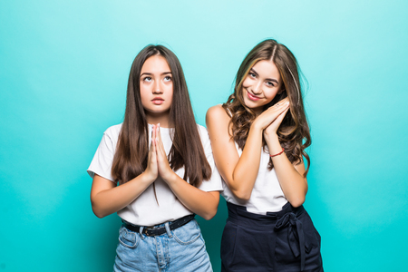 Two pleased girls in sweaters hugging to each other and looking at the camera over white background