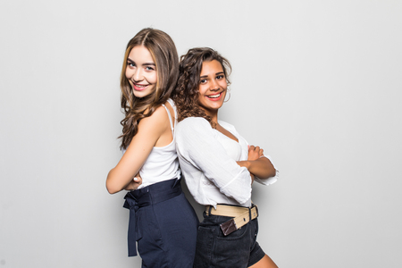 Two young girls stand back to back and smiling to camera on gray background.の写真素材