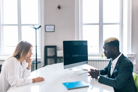 African American and Caucasian managers communicating at office table. Black man listening with attention to colleague talking at company meeting.の写真素材