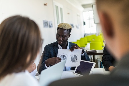 handsome young african american businessman presenting figures at a meeting with teamの写真素材
