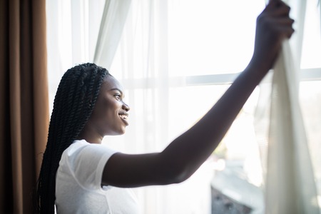 Back view of stretching african woman with curly hair in bed near window in the morning