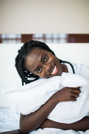 Beautiful Black Woman With Smiling Face Having Fun And Hugging Pillow Isolated On White Backgroundの写真素材