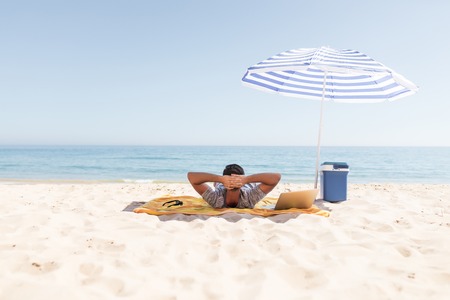 Young man is resting under umbrella on a sun overlooking the sea on the beachの写真素材