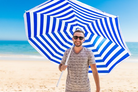 The man in sunglasses with sun umbrella in hands on the beach.の写真素材