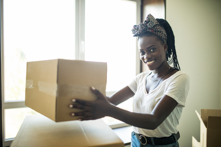 Attractive young african woman is moving, looking at each other and smiling while standing among cardboard boxes.の写真素材