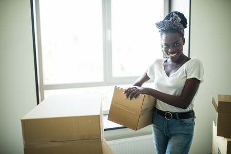 Young african woman moving into new apartment holding cardboard boxes with belongingsの写真素材