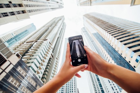 Close up of woman hands take phone on the phone of skycrapers in modern arhitecture city.の写真素材