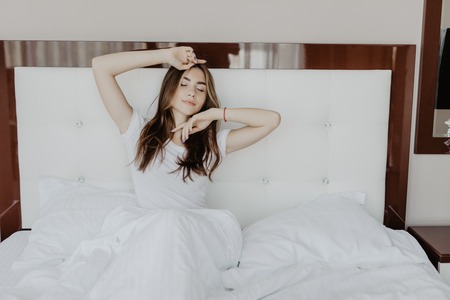 Beautiful woman waking up in her bed in the bedroom, she is stretching and smilingの写真素材