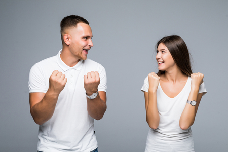 Portrait of glad positive couple in casual outfits with raised arms celebrating victory isolated on grey backgroundの写真素材