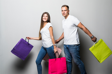 Happy young couple with shopping bags embracing and looking away isolated on whiteの写真素材