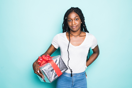 Portrait of joyous woman 20s with afro hairdo holding gift box and smiling in happiness isolated over blue backgroundの写真素材