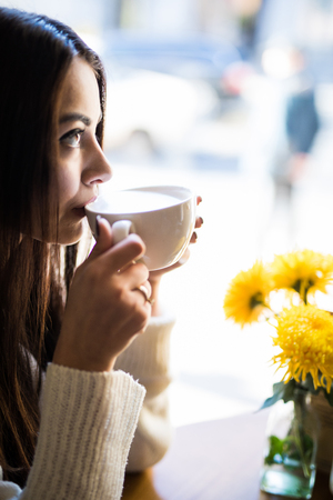 Smiling young woman drinking coffee at cafeの写真素材