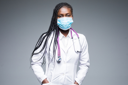 Close up of african female nurse wearing mask and hair net on gray backgroundの写真素材