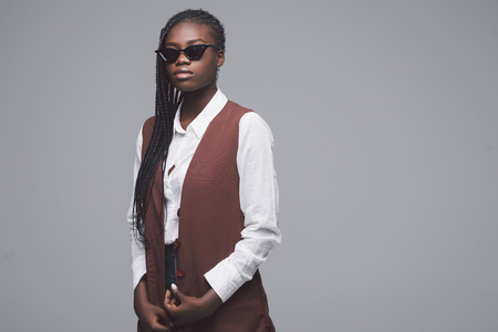 Portrait of a african woman wearing sunglasses and fashionable clothes standing against a wall.の写真素材