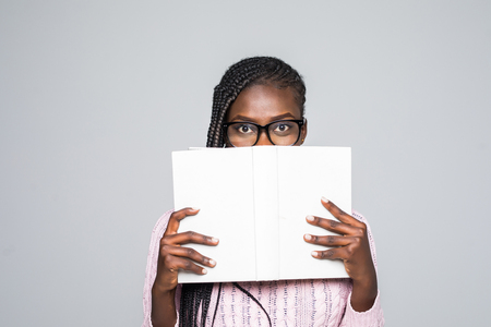 Portrait of a young woman hiding behind a book with glasses on a gray backgroundの写真素材