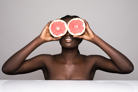 Beauty african woman with orange citrus grapefruit cover eyes with healthy skin body. Attractive fresh vitamin. Studio shot.の写真素材