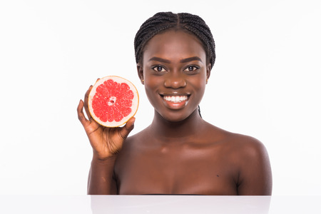 Photo of african american girl holding a half of pomelo in front of her face and smiling on white background. Skin care and beauty concept.の写真素材