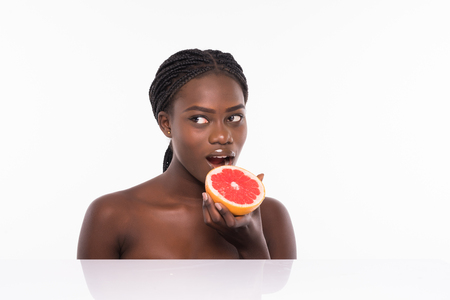 Photo of african american girl holding a half of pomelo in front of her face and smiling on white background. Skin care and beauty concept.の写真素材