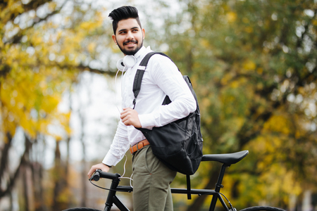 Casual handsome businessman going to work by bicycle. He is pushing bikeand drinking coffee to go.