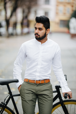 Happy young indian man dressed in shirt standing with a fixed gear bicycleの写真素材