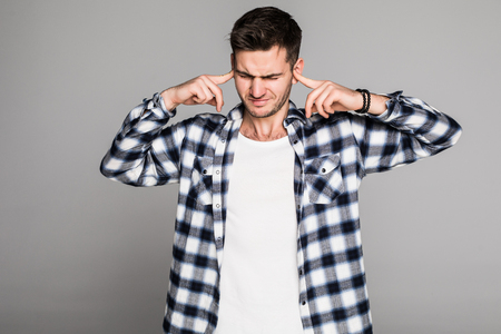 Close up of a stressed young brunet man closing his ears with hands isolated on gray backgroundの写真素材