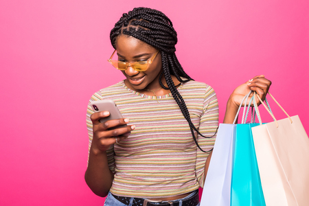 Happy shopping woman texting on her cell phone over pink backgroundの写真素材