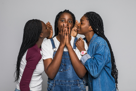 Three african girl friends sharing gossip isolated on white backgroundの写真素材