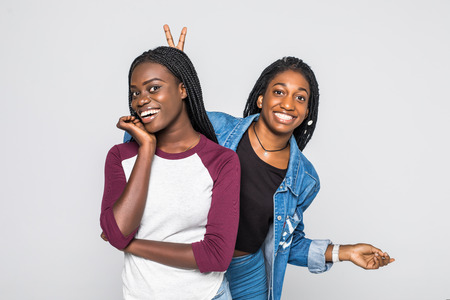 Sensual african lady having fun with her best friend. Adorable african girls in casual clothes standing on white background.の写真素材