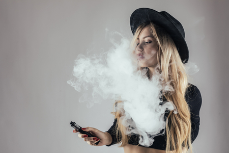 Young woman in hat with e-cigarette make smoke cloud isolated on white backgroundの写真素材