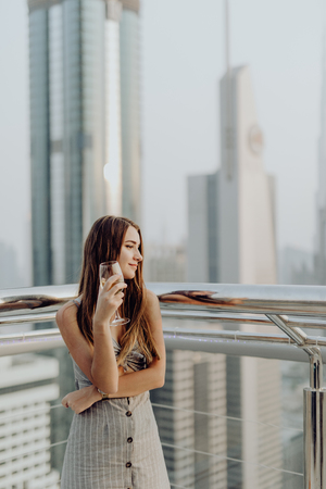 Young beauty woman with glass of white wine on skyscrapers of Dubai background.の写真素材